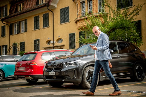 Mann läuft mit Smartphone in der Hand an 3 Autos vorbei