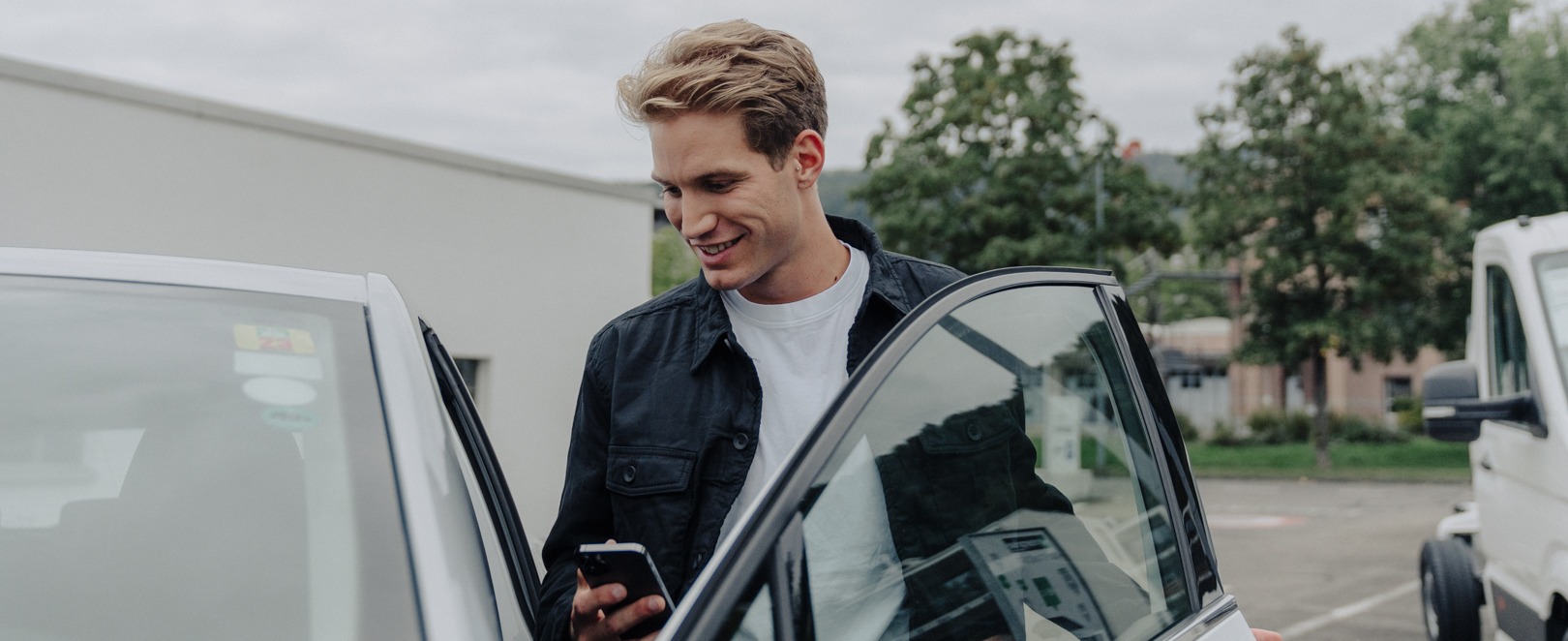 Mann mit Smartphone in der Hand öffnet Autotüre