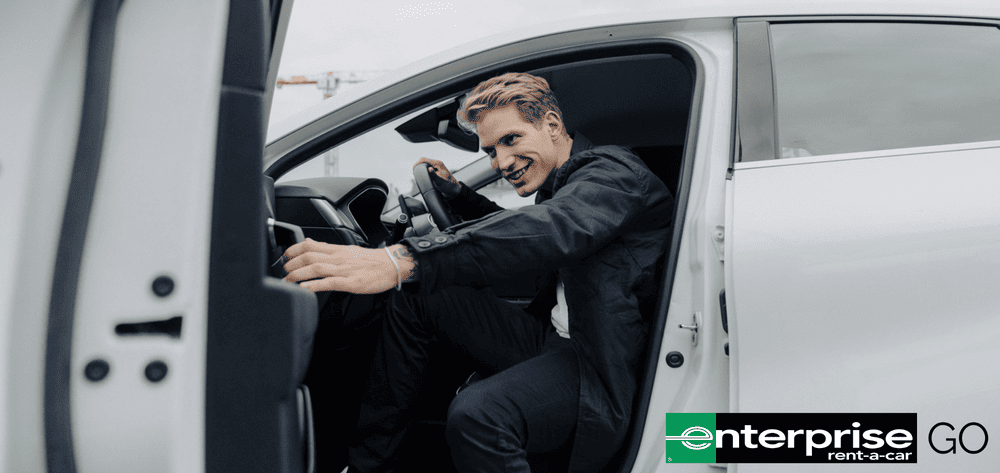 Smiling man sits in grey car and closes the door